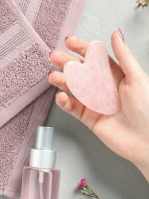 Woman with rose quartz gua sha tool at white table, top view